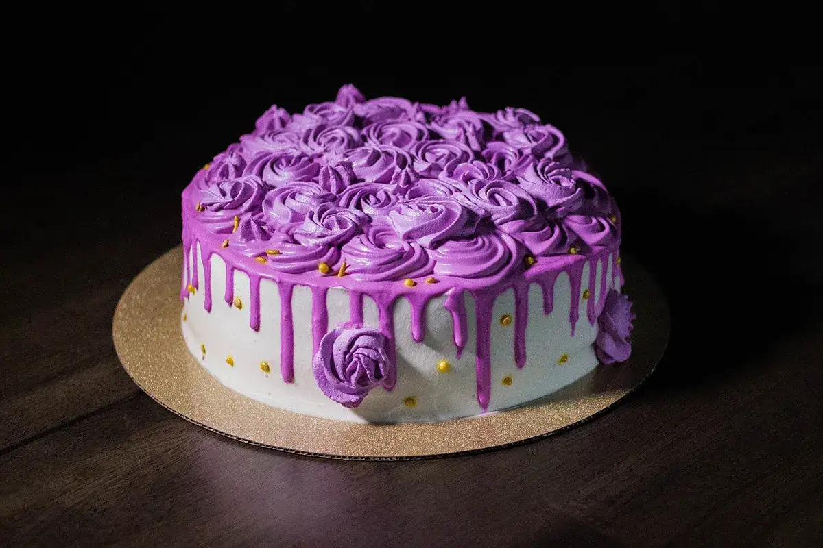 Torta decorata con abbondante crema al burro viola a forma di rose e gocce rosa shocking.