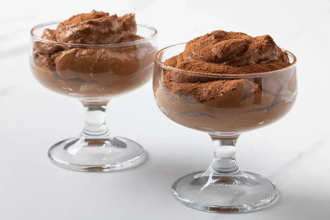 Due coppe di vetro piene di soffice mousse al cioccolato, spolverate con cacao amaro.