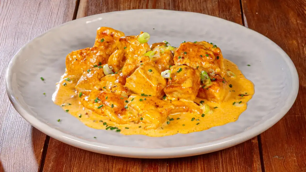 Succulento pollo alla paprika in cremosa salsa, guarnito con erba cipollina fresca, servito su un piatto grigio.