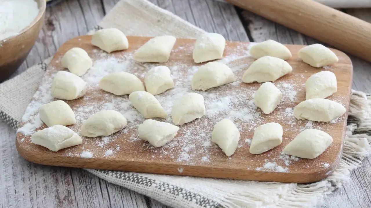 Gnocchi di ricotta freschi, pronti per essere cotti, spolverati di farina su un tagliere di legno.