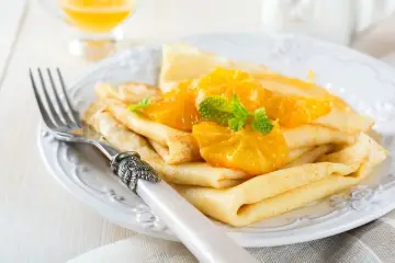 Deliziose crepes senza uova, guarnite con spicchi d'arancia succosa e foglioline di menta fresca. Un piatto leggero e gustoso.