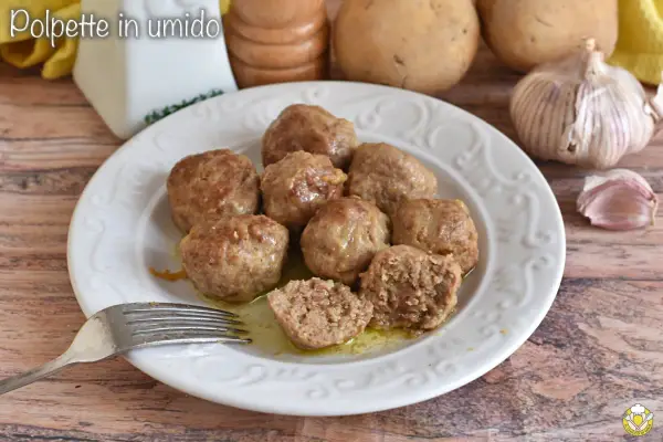 Piatto di polpette in bianco, morbide e succulente, pronte per essere gustate. Sullo sfondo patate e aglio.
