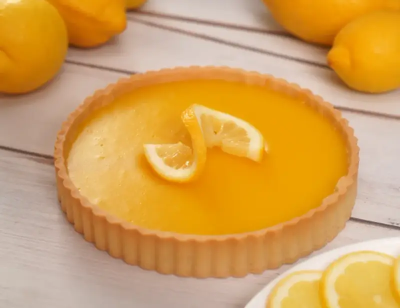 Una deliziosa crostata al limone, con la sua crema gialla brillante e decorata con spicchi di limone fresco.