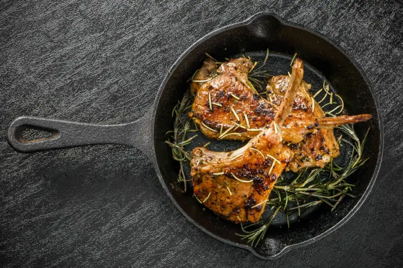 Tre succulenti costolette di agnello in padella, guarnite con rosmarino fresco, pronte per essere gustate.