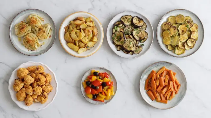 Sette piatti di verdure in friggitrice ad aria: finocchi gratinati, patate arrosto, melanzane, zucchine, cavolfiore fritto, peperoni e carote.