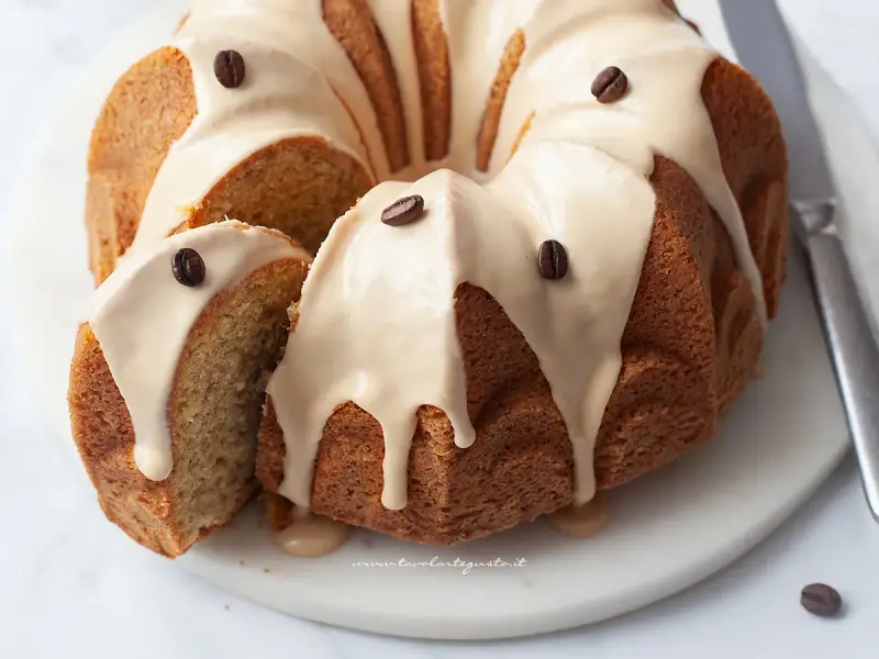 Deliziosa torta al caffè con glassa chiara e chicchi di caffè come decorazione. Una fetta è stata tagliata, mostrando la morbidezza dell'interno.