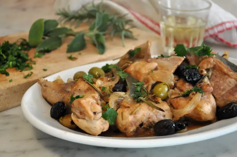Un saporito coniglio alla cacciatora in bianco, con olive verdi e nere, cipolle e rosmarino, pronto per essere gustato.
